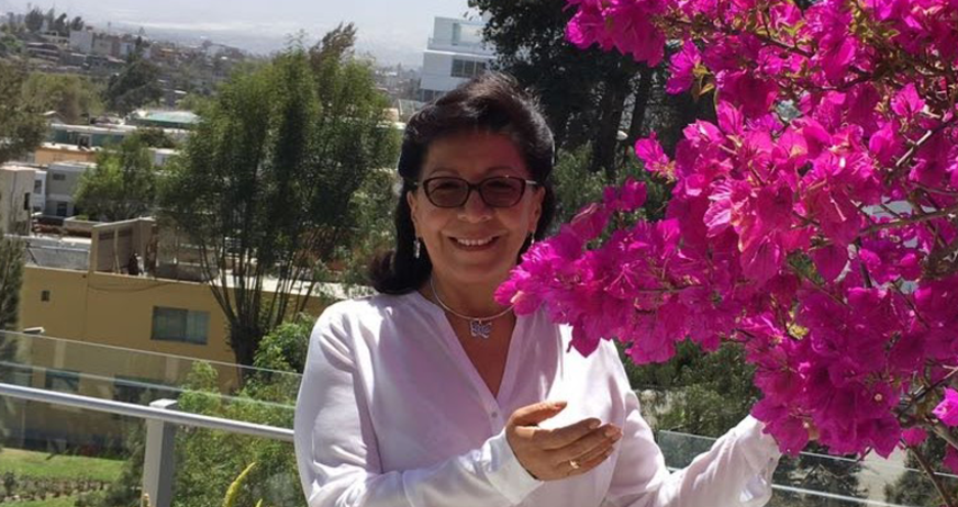 Smiling woman in white shirt holding vibrant pink flowers with city view in the background.